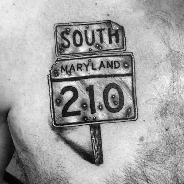Black and grey tattoo of a weathered 'South Maryland 210' road sign with a rustic, worn look, placed on the upper chest.
