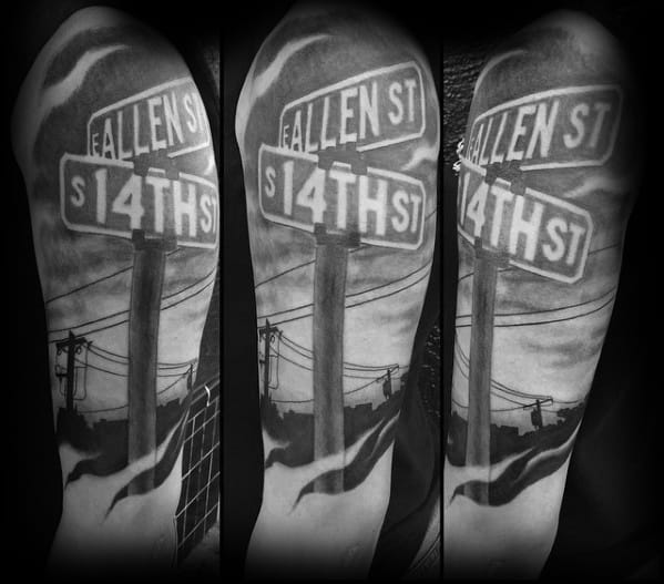 Black and grey tattoo of a realistic street signpost featuring 'Fallen St' and 'S 14th St,' set against a cloudy sky with power lines.
