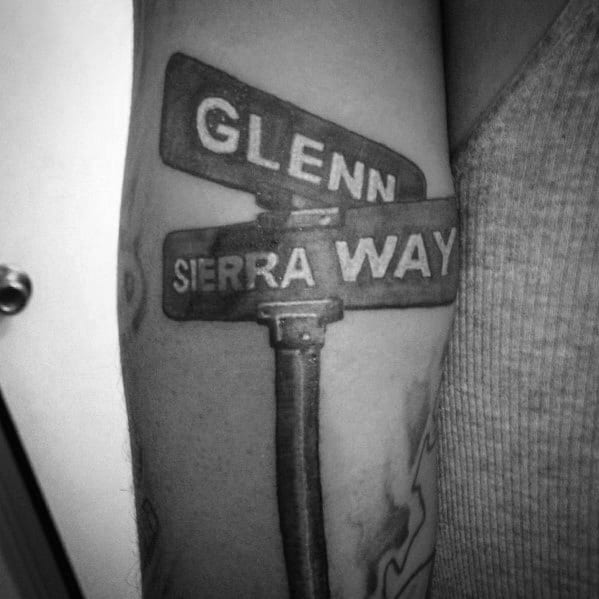 Black and grey tattoo of a detailed street signpost featuring 'Glenn' and 'Sierra Way,' with bold lettering and realistic shading.