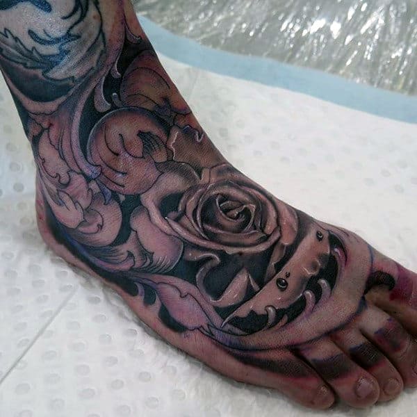A foot with a detailed black and gray tattoo featuring a rose and intricate ornamental designs