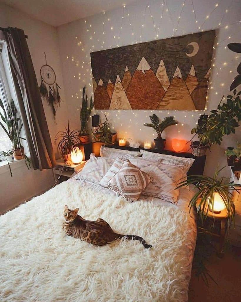 Cozy bedroom with a fluffy bed, cat, mountain tapestry, plants, and warm string lights