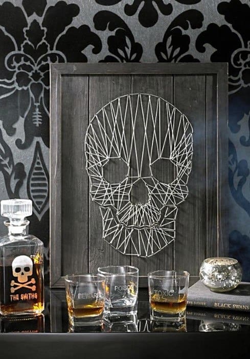 String art skull with whiskey set on a table, against a dark floral wallpaper background