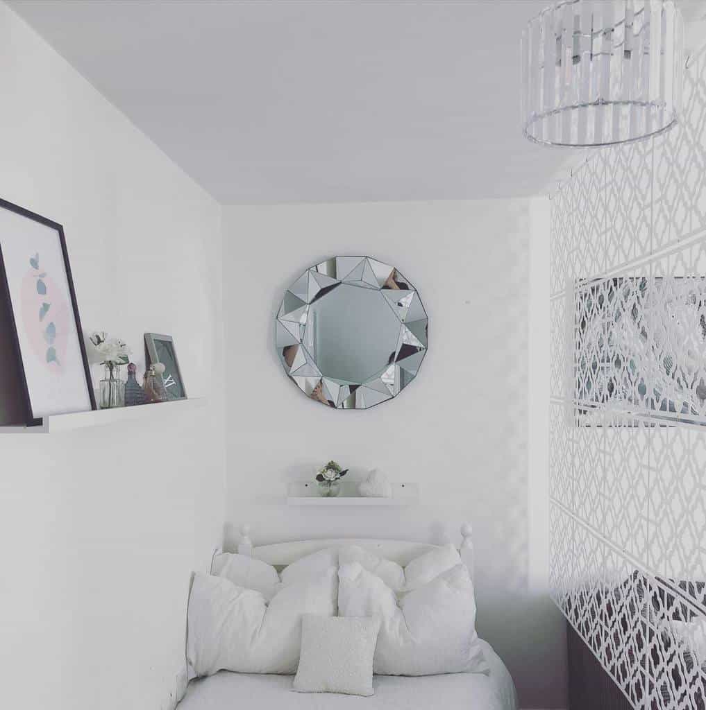 White studio apartment bedroom with decorative mirror, cozy bedding, and minimalist decor.