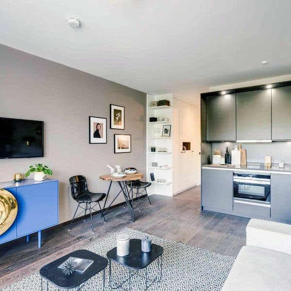 Modern studio apartment with sleek grey cabinetry, a vibrant blue console, and minimalist decor for a cozy yet stylish feel.