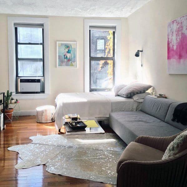 Cozy studio with natural light, gray sofa, wooden floors, and colorful wall art.