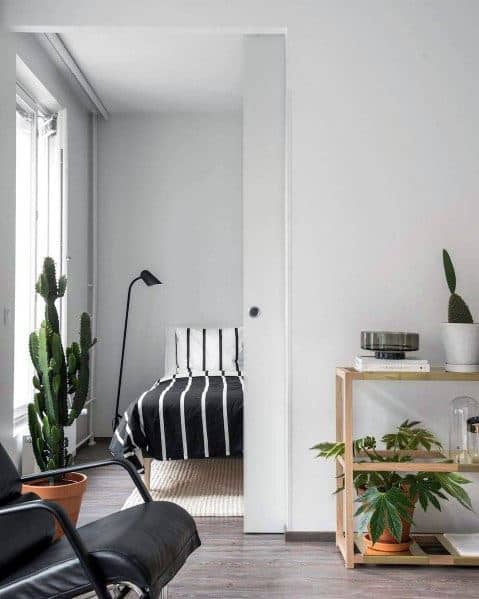 Minimalist studio with striped bedding, sliding door, and vibrant potted plants.