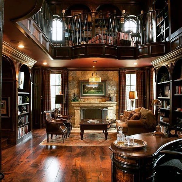 Luxurious library with dark wood, bookshelves, plush seating, and a stone fireplace under a mezzanine