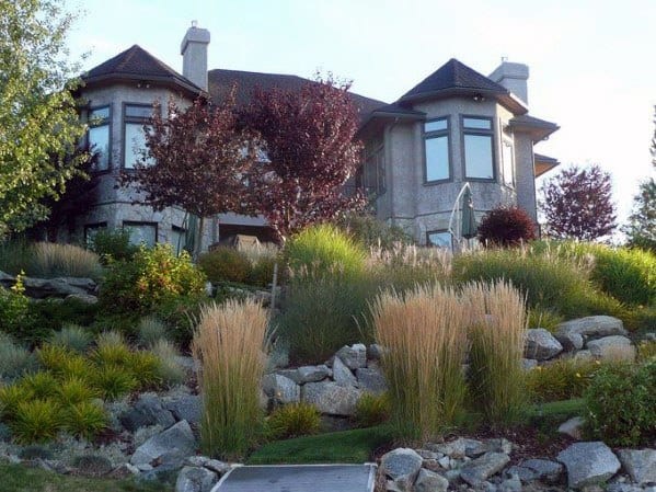 Sloped backyard with ornamental grasses, natural boulders, and lush shrubs complementing a modern home for a stunning landscape design