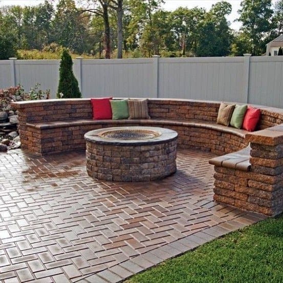 Brick fire pit with seating on a paved patio and colorful cushions