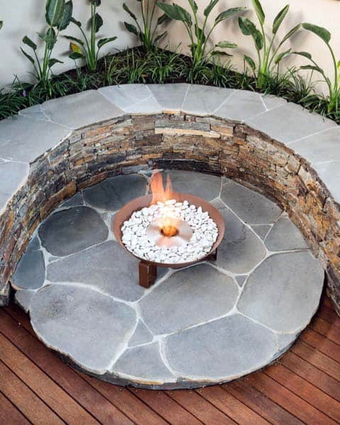 Circular stone patio with a fire pit surrounded by plants and wooden decking