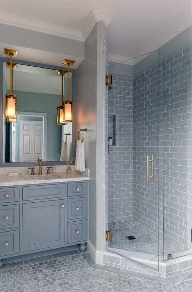 Modern corner bathroom with a blue vanity, large mirror, glass shower, and soft lighting from two pendant lights