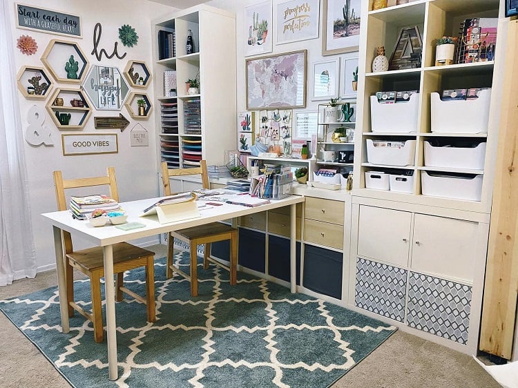 Craft room with organized shelves, a table with chairs, wall art, and colorful paper storage on a patterned rug