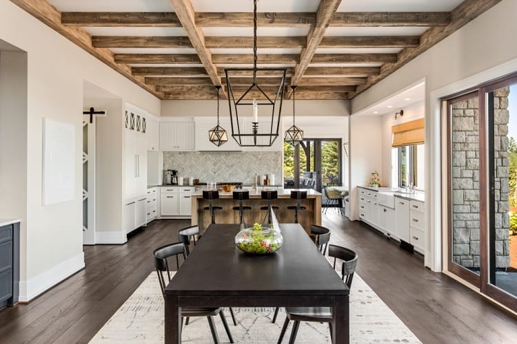 Spacious kitchen and dining area with wooden beams, modern fixtures, and a large table centerpiece under a high ceiling