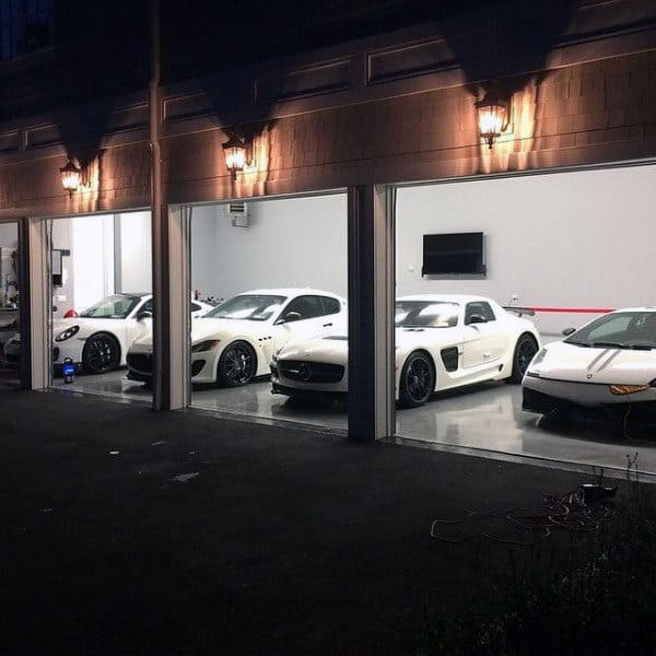 Sophisticated garage featuring a lineup of luxurious white supercars, illuminated by elegant exterior lights.