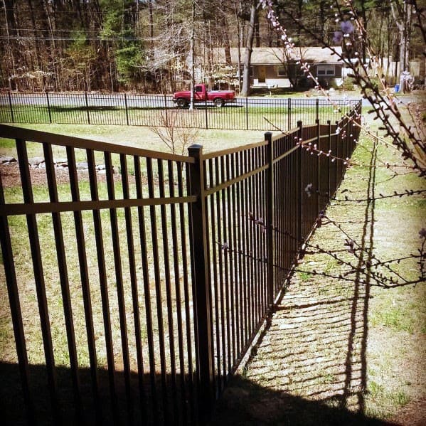 A sturdy metal fence encloses a grassy yard, with trees and a red truck visible beyond