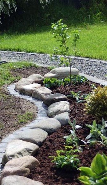 A winding stone border around a garden bed with newly planted shrubs and a young tree, creating a natural path in the landscape