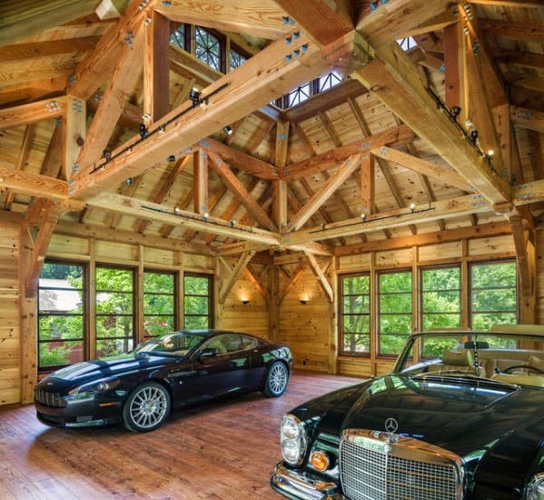 Luxury garage with exposed wood trusses, large windows, and vintage cars on polished floors.