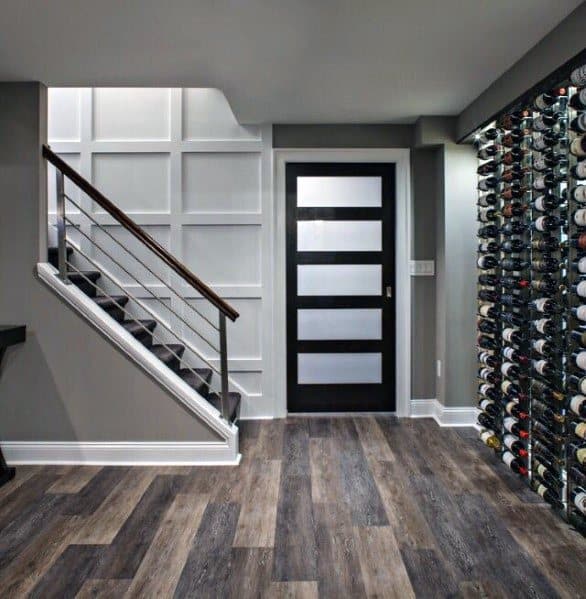 Modern basement with wooden staircase, horizontal metal handrails, and built-in wine rack.