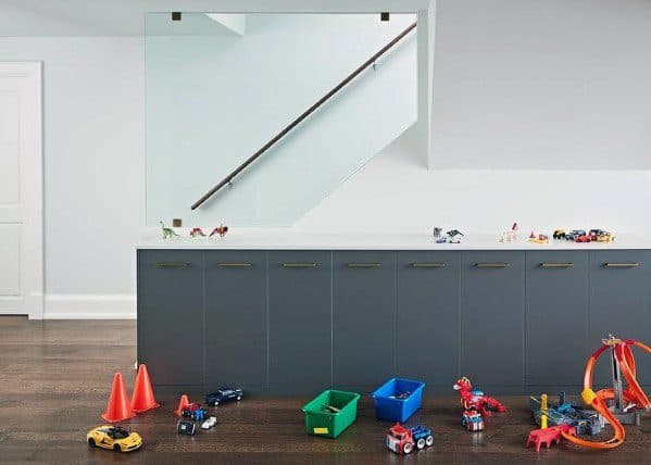 Children's play area with toys scattered on dark wooden floors and wall-mounted handrail in the background.