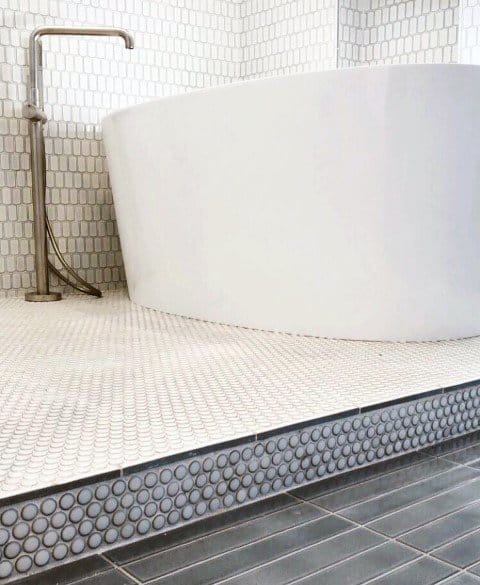 Freestanding tub with white penny round tiles on floor and raised platform edge.