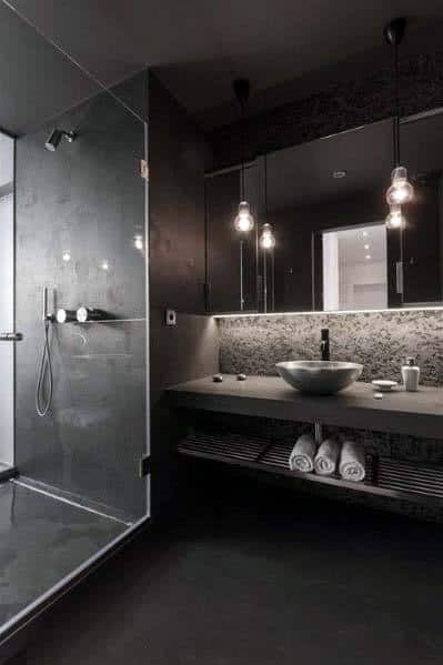 Modern black bathroom with glass shower, vessel sink, and hanging pendant lights.