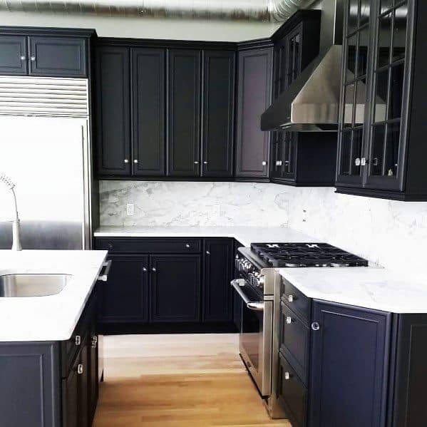 Black kitchen cabinets with white countertops, marble backsplash, and sleek finishes.
