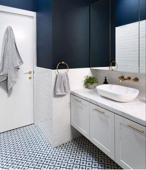 Bathroom with navy blue upper walls, white vanity, gold fixtures, and patterned tile flooring.
