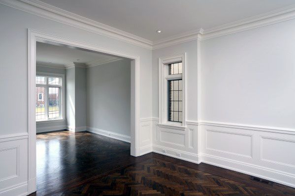 Empty room with white walls, a dark wood herringbone floor, chair rail, and large windows letting in natural light