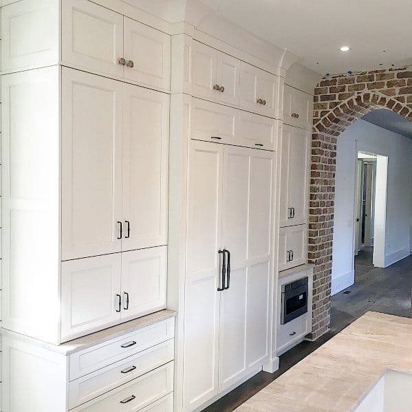 Elegant kitchen with white cabinetry and crown molding, complemented by a charming brick archway, creating a refined and spacious feel