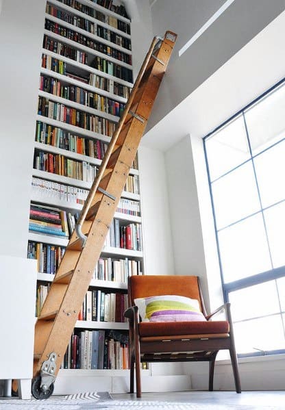 Tall wooden ladder against a massive bookshelf, beside a window and chair