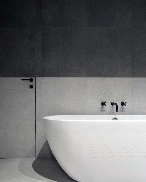 Minimalist bathroom with a white freestanding tub against sleek two-tone grey walls and black fixtures.
