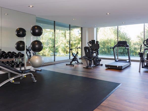Modern home gym with hardwood and rubber flooring, cardio machines, and large glass windows.