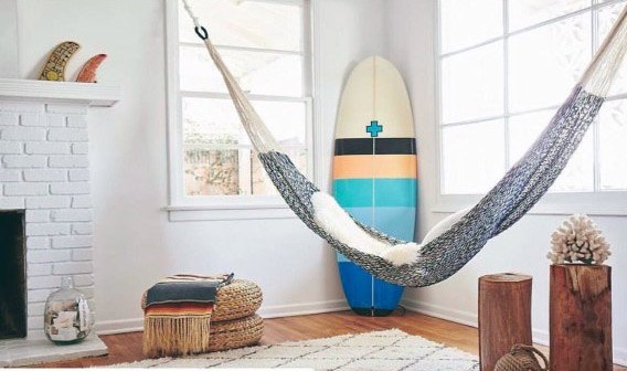 Indoor hammock in a bright room with a surfboard, white brick fireplace, and cozy decor accents.