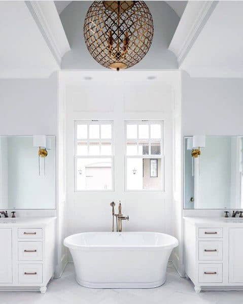 Bright white bathroom with freestanding tub, double vanities, and Moroccan wrought iron chandelier.