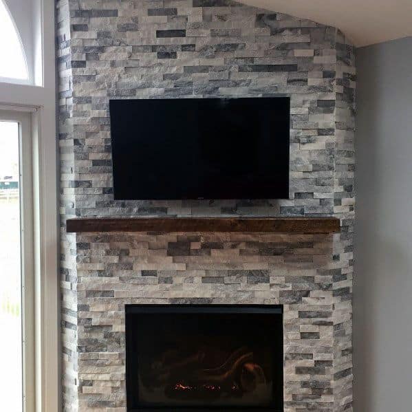 Stacked stone fireplace with a dark wooden mantel and TV above
