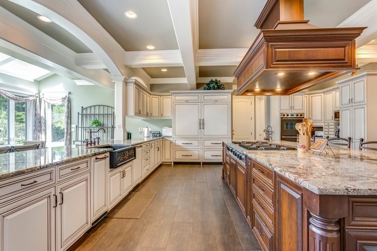 A stunning kitchen with a coffered ceiling, elegant cabinetry, granite countertops, and large windows providing plenty of natural light, creating a sophisticated and spacious atmosphere