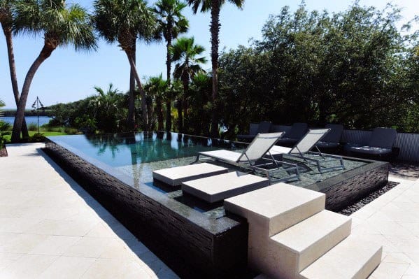 A stunning modern infinity pool featuring sleek black tiles and minimalist stepping stones, surrounded by lush palm trees for a tropical retreat feel.