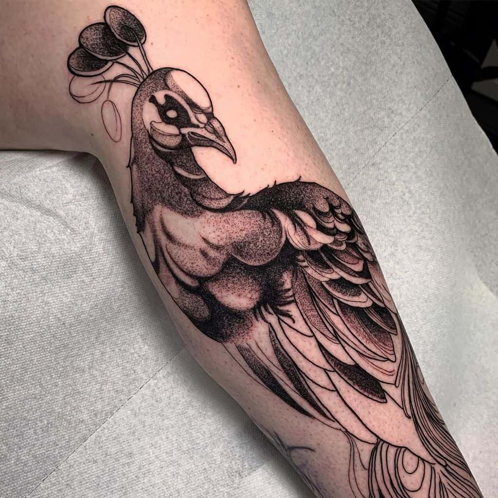 Black and white peacock tattoo with detailed shading, showcasing a realistic design of the bird on the arm.