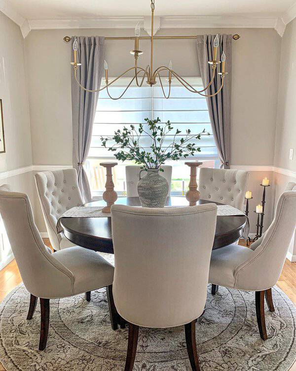 Elegant dining room with tufted chairs, a round table, a gold chandelier, and soft gray curtains.