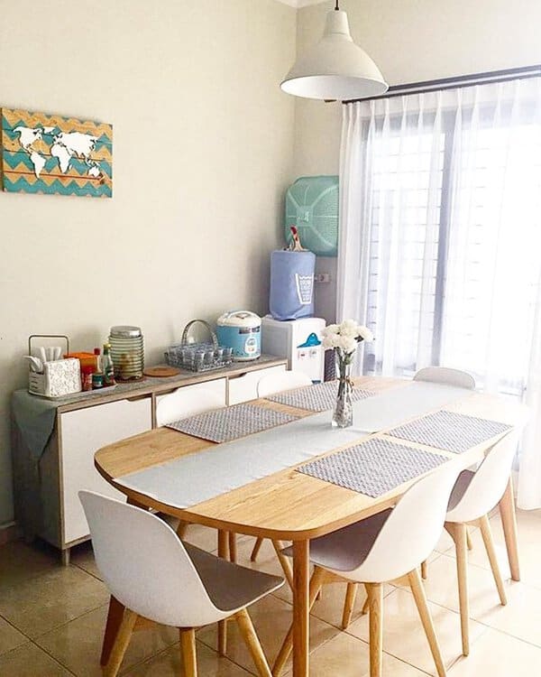 Modern dining room with a wooden table, white chairs, and sheer curtains letting in natural light.