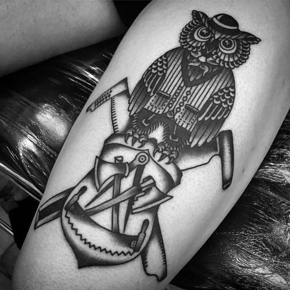 Black and gray tattoo of a dressed-up owl sitting on crossed carpentry tools, symbolizing wisdom, craftsmanship, and mastery of the trade.