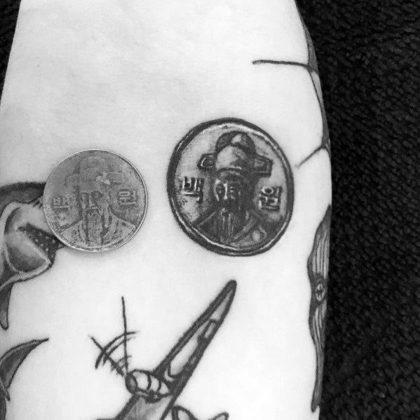 Realistic tattoo of a South Korean 100 won coin, placed beside an actual coin for comparison, featuring intricate shading and fine details.