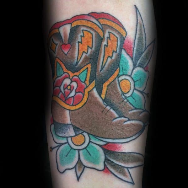 Tattoo of a pair of cowboy boots with bold floral designs, vibrant colors, and traditional Western patterns, symbolizing heritage and style.