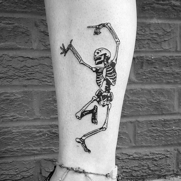 Dancing skeleton tattoo with bold black ink, raised arms, and a playful pose, creating a striking and energetic design on the lower leg.
