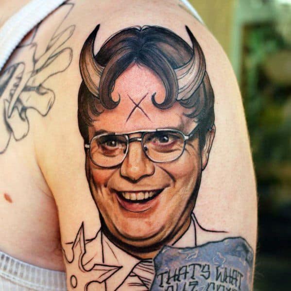 Tattoo of Dwight Schrute with devilish curved horns, wearing glasses and smiling mischievously, featuring bold shading and "That's What" text.