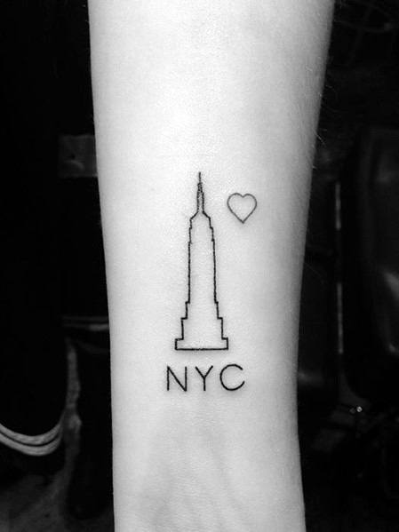 Minimalist Empire State Building outline tattoo with a small heart and "NYC" lettering on a man's wrist.