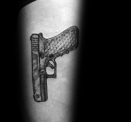 Black and grey tattoo of a Glock pistol on the arm, featuring intricate shading and a textured grip design for a detailed and realistic look.