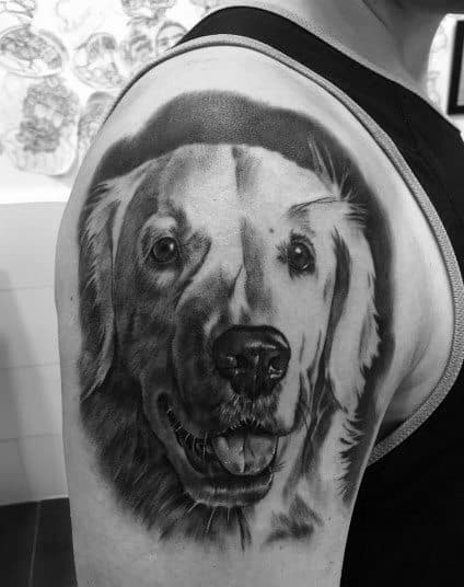 Realistic black and grey Golden Retriever tattoo on the upper arm, featuring detailed fur shading and a joyful expression for a lifelike tribute.