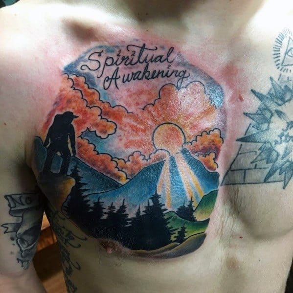 Vibrant chest tattoo of a hiker overlooking mountains with a sunrise and 'Spiritual Awakening' text, symbolizing personal growth and adventure.