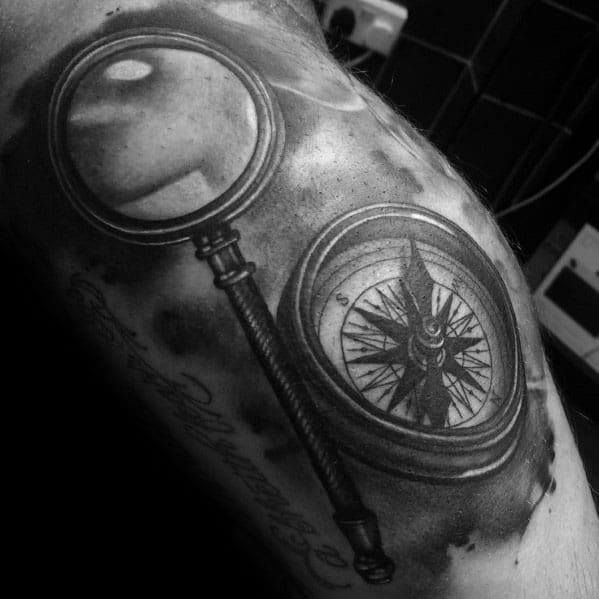 Tattoo featuring a magnifying glass and a compass, designed with deep shading and realistic details for a bold and adventurous exploration-themed look.